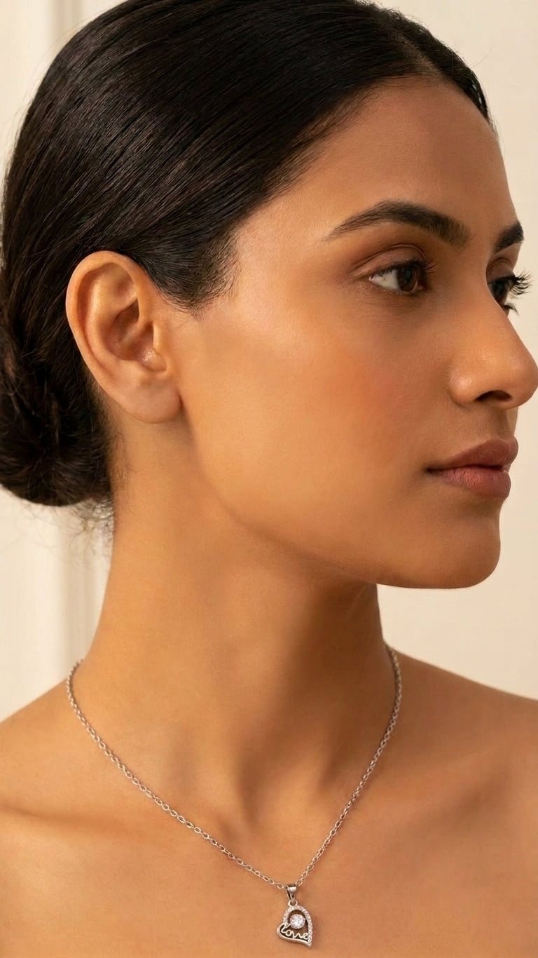 Woman wearing silver CZ love heart pendant necklace with cream silk blouse in elegant setting – AureliaBlends