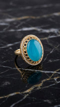 Turquoise oval stone gold statement ring on black marble surface showing scalloped lattice halo setting and gold band – AureliaBlends