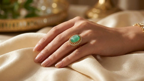 Emerald green stone gold statement ring worn on woman's hand resting on cream silk fabric – bridal jewelry gift for her – AureliaBlends