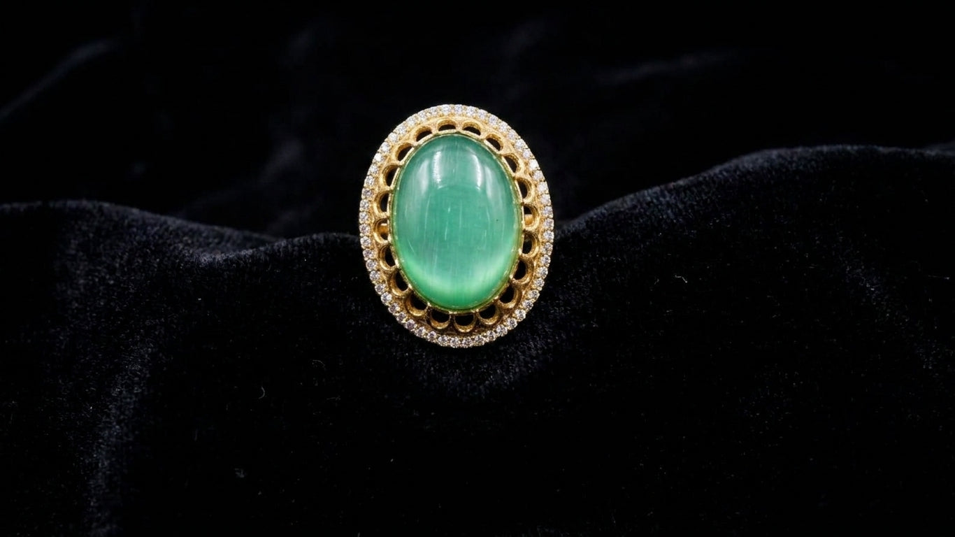 Close-up front view of emerald green cabochon oval stone gold-plated statement ring with cubic zirconia pavé halo on black velvet – AureliaBlends