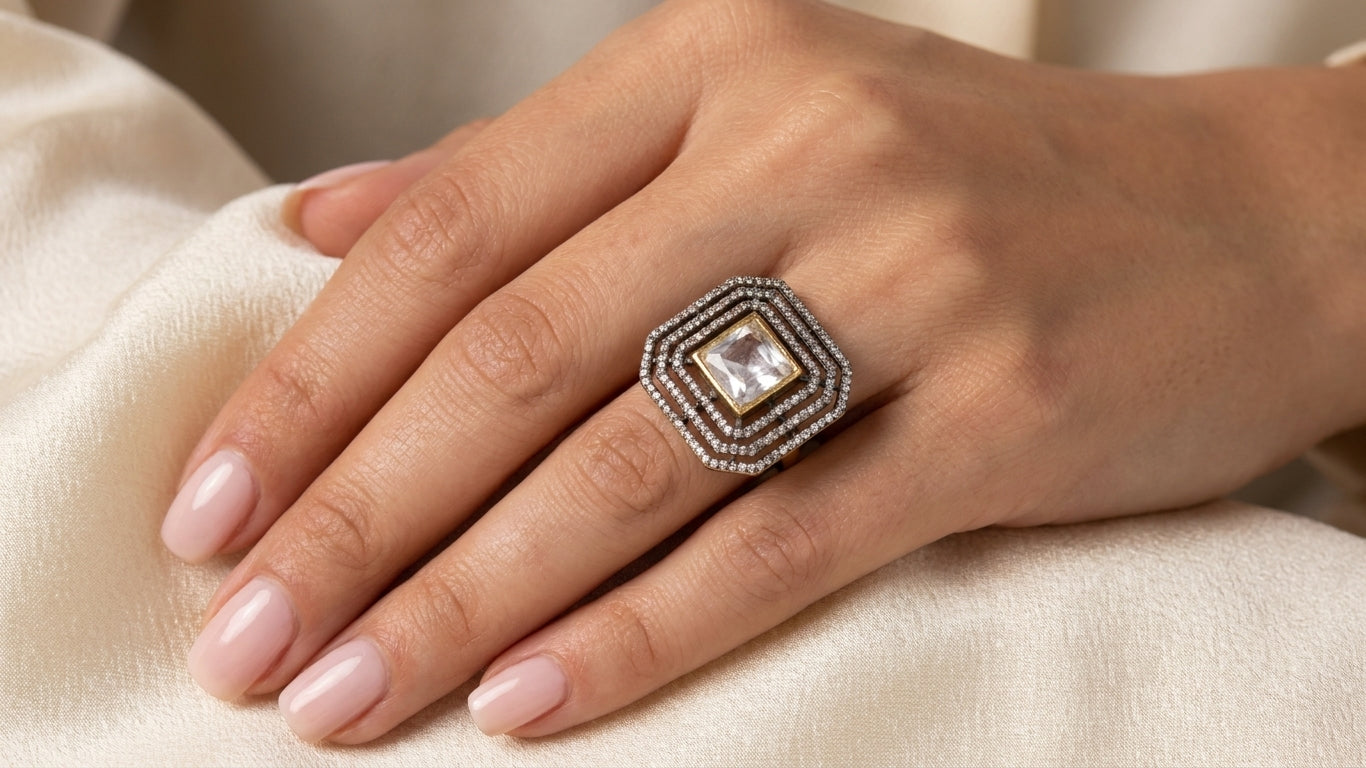 Crystal square stone gold-plated multi-row cubic zirconia statement ring worn on woman’s hand on cream silk fabric – AureliaBlends