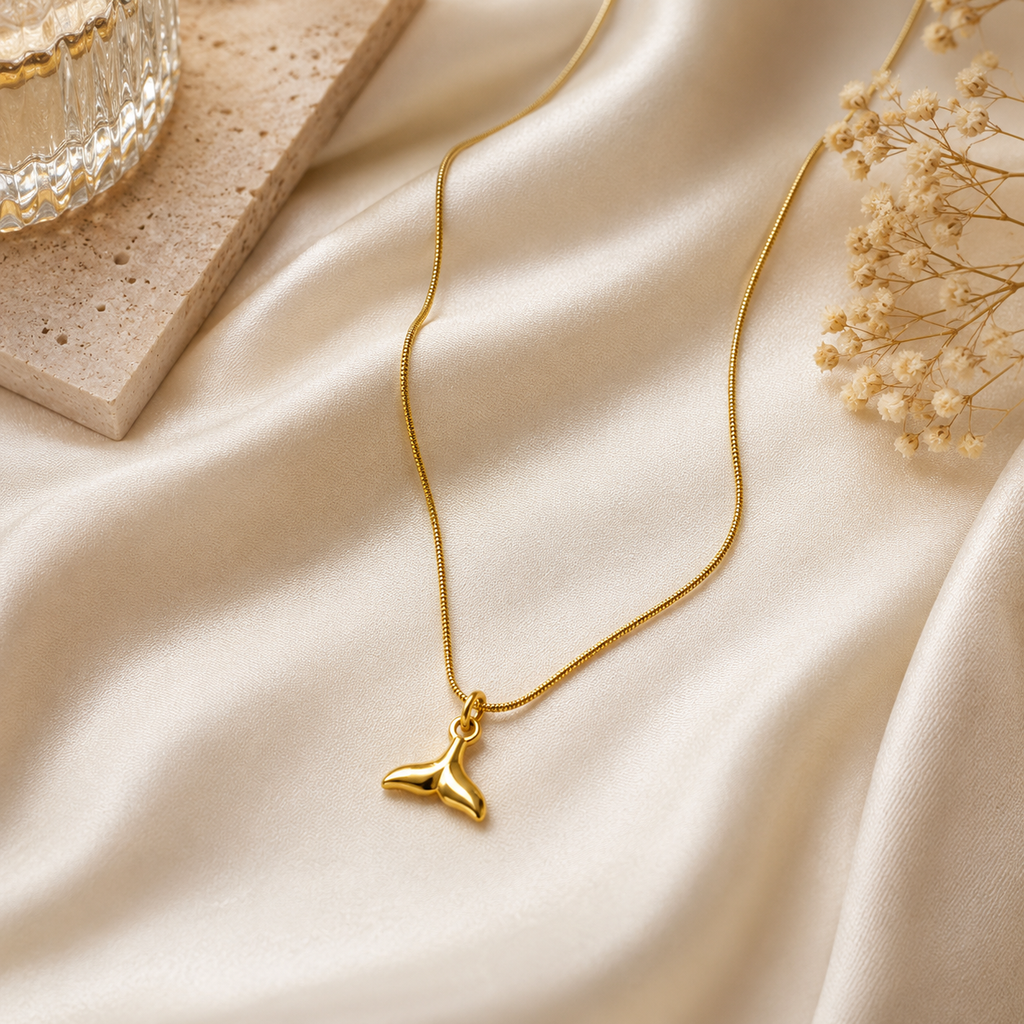 Gold sculptural whale tail mermaid charm pendant necklace on box chain on black gift box with dried flowers on dark background – statement necklace evening wear