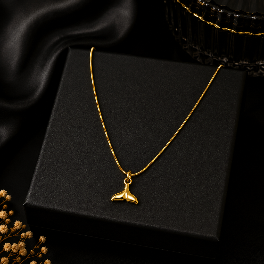 Gold whale tail mermaid pendant necklace displayed on black velvet jewelry bust in luxury jewellery boutique with 'Timeless Elegance' branding card and candlelight – wedding guest necklace USA UK