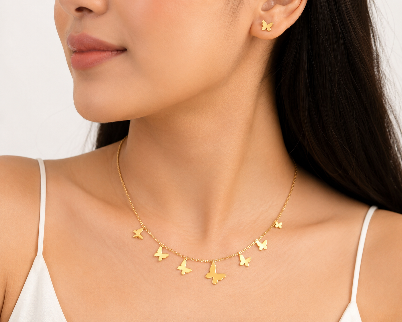 Woman wearing gold multi-butterfly charm dangle necklace and butterfly stud earrings set at collarbone in white cami top – dainty gold butterfly jewelry set AureliaBlends