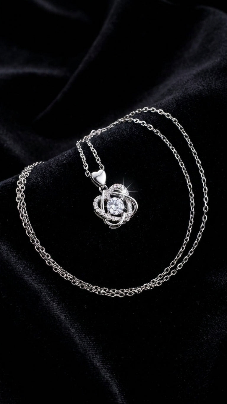 Close-up of silver CZ love knot pendant necklace with round-cut cubic zirconia centre stone and heart bail on white background – AureliaBlends