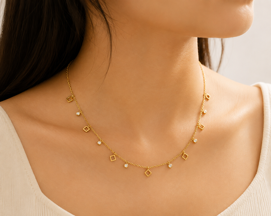 Gold geometric square and CZ bezel charm dangle necklace on black velvet jewelry bust against dark Art Deco gold patterned background – statement necklace evening wear AureliaBlends