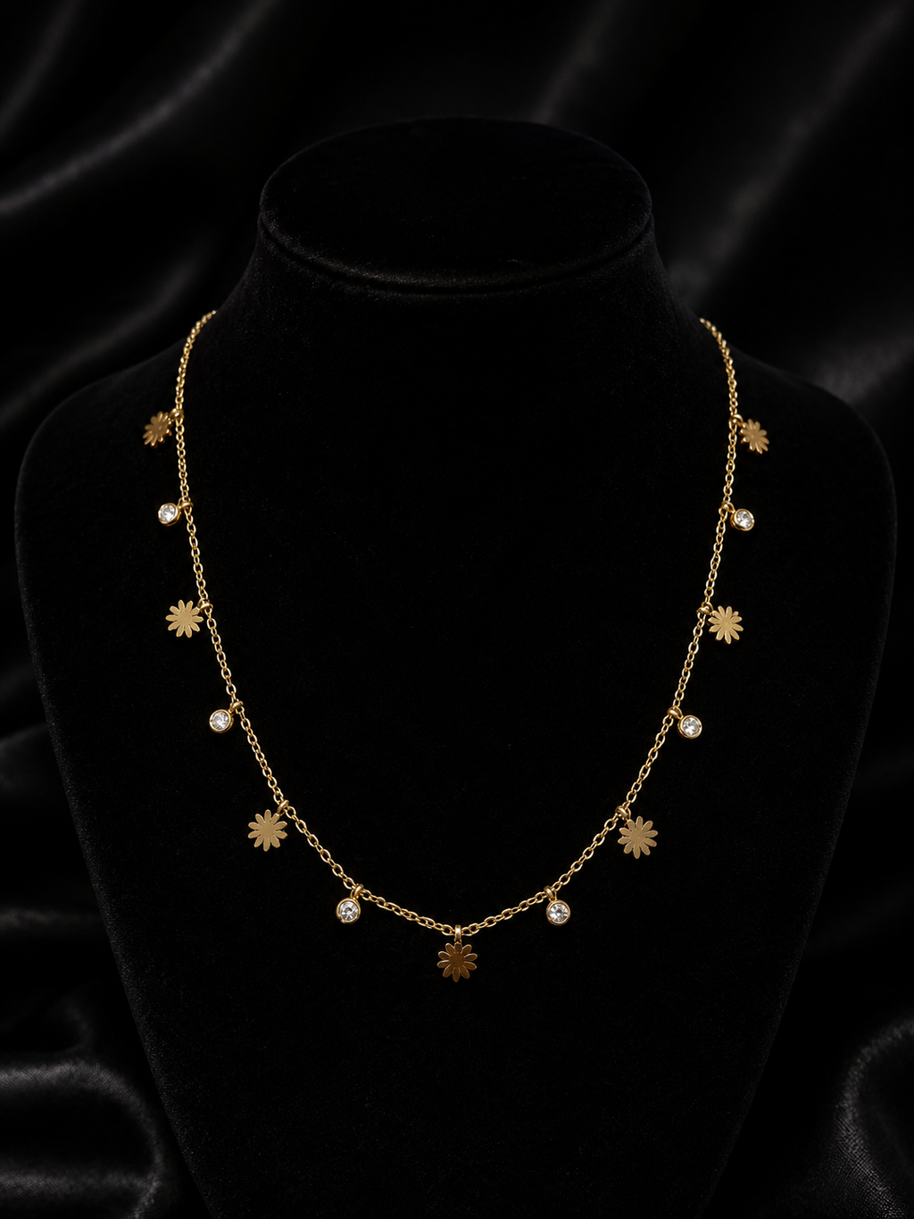Gold daisy flower and cubic zirconia drop necklace laid flat on champagne satin fabric – dainty floral charm necklace AureliaBlends