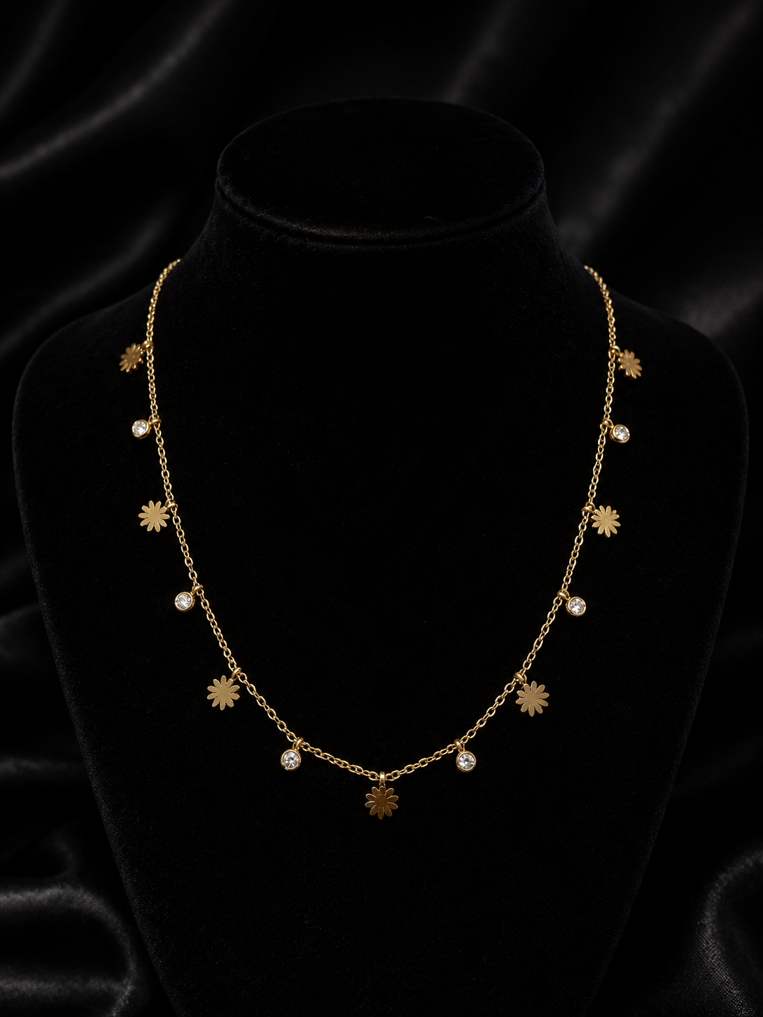 Gold daisy flower and cubic zirconia drop necklace laid flat on champagne satin fabric – dainty floral charm necklace AureliaBlends