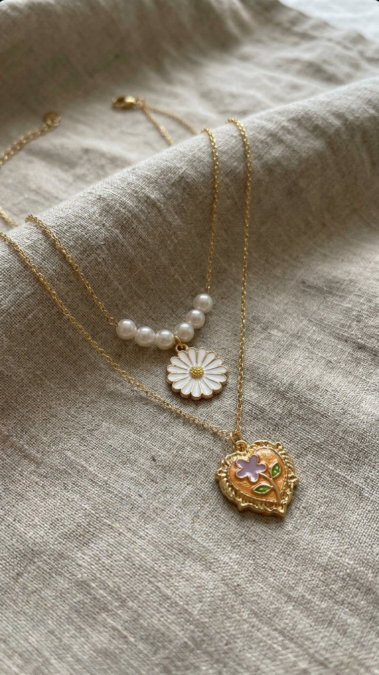 Close-up of white enamel daisy pendant on pearl station chain and orange enamel floral heart locket on gold cable chain – 18K gold-plated layered necklace detail by AureliaBlends