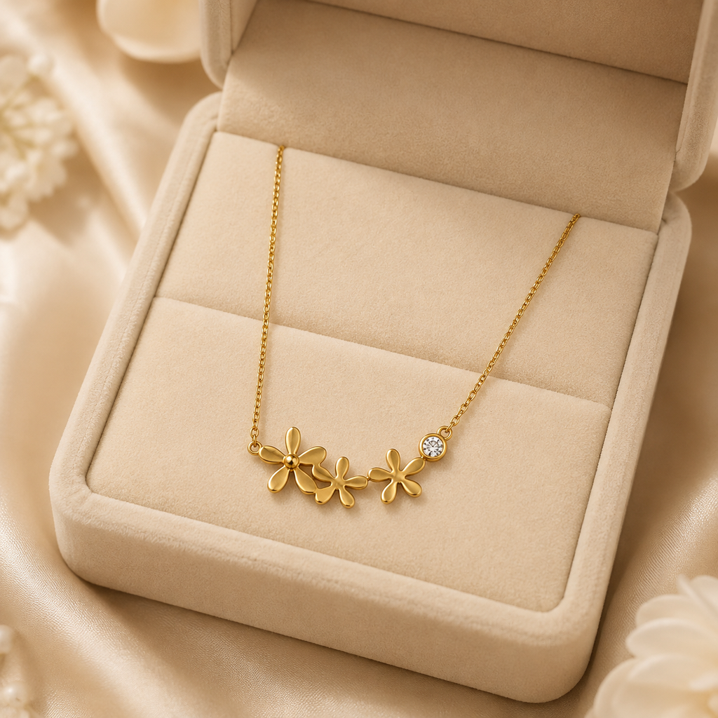Gold triple daisy flower and CZ pendant necklace flat lay surrounded by blush pink garden roses, ranunculus and baby’s breath on cream surface – romantic floral gold necklace gift AureliaBlends