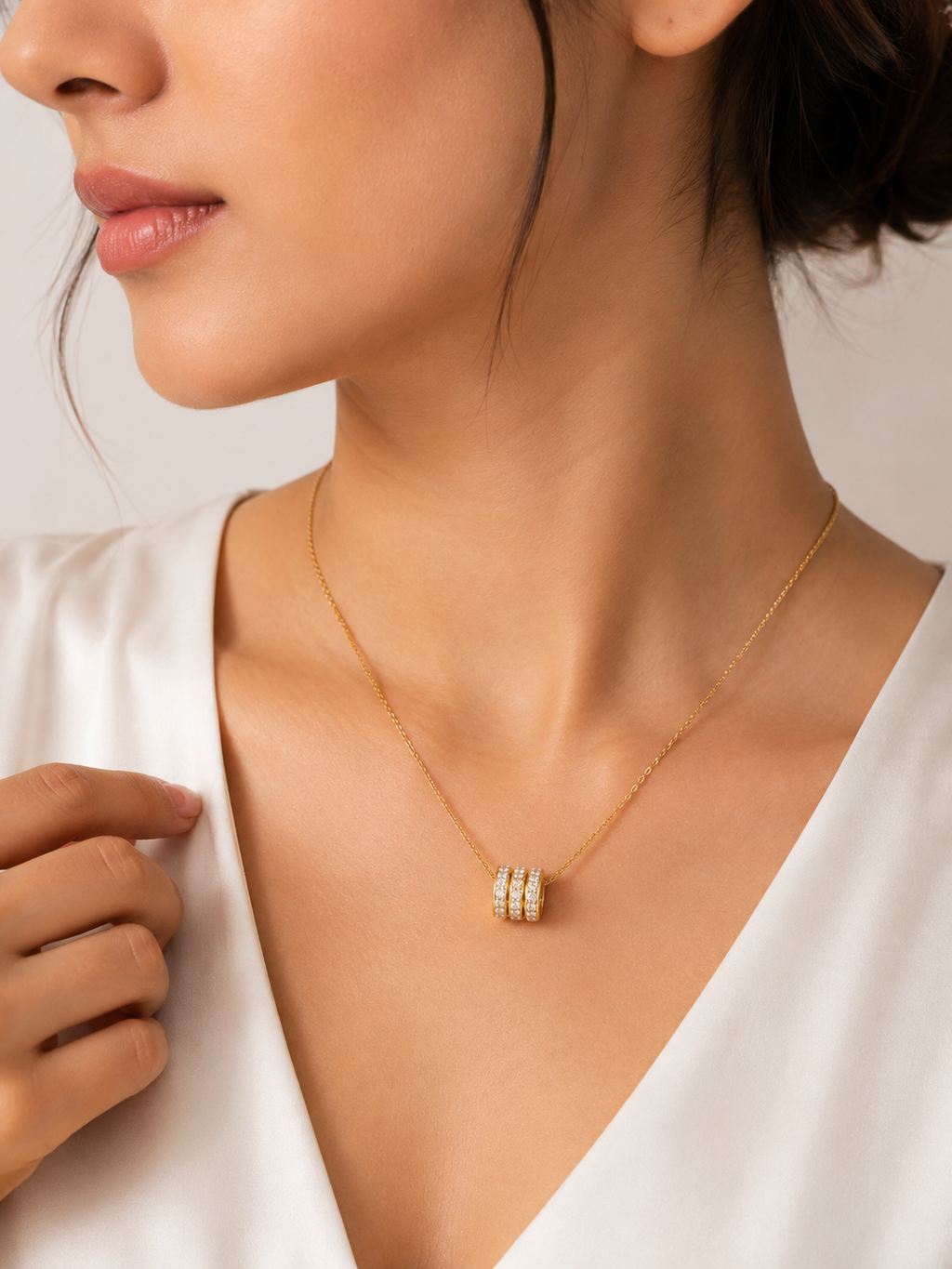 Gold triple pavé CZ crystal ring bead barrel pendant necklace flat lay on blush cream satin with dried pink flowers, crystal dish and gold wave ornament – romantic CZ necklace gift AureliaBlends