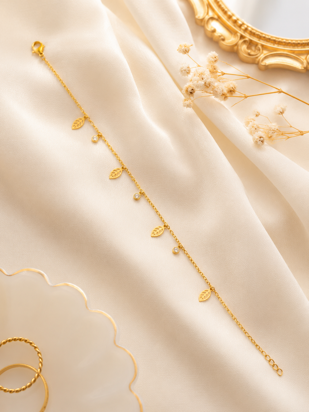 Dainty gold leaf and CZ dangle bracelet flat lay on cream silk with gold mirror frame and dried flowers – AureliaBlends