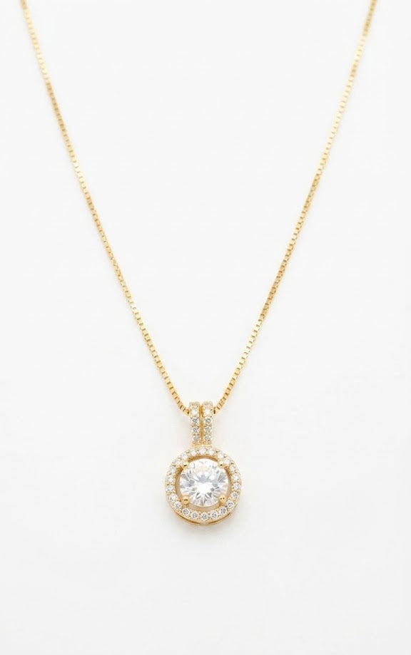 Gold round halo CZ diamond solitaire pendant necklace flat lay on cream linen fabric with white gardenia flower and Chanel No.5 perfume bottle – 18K gold-plated pavé halo necklace by AureliaBlends
