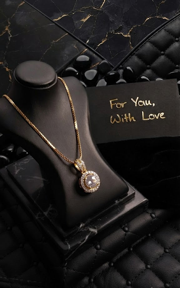 Gold round halo CZ diamond solitaire pendant necklace flat lay on cream surface with dried botanicals and gold accessories – dainty diamond-look halo pendant necklace AureliaBlends