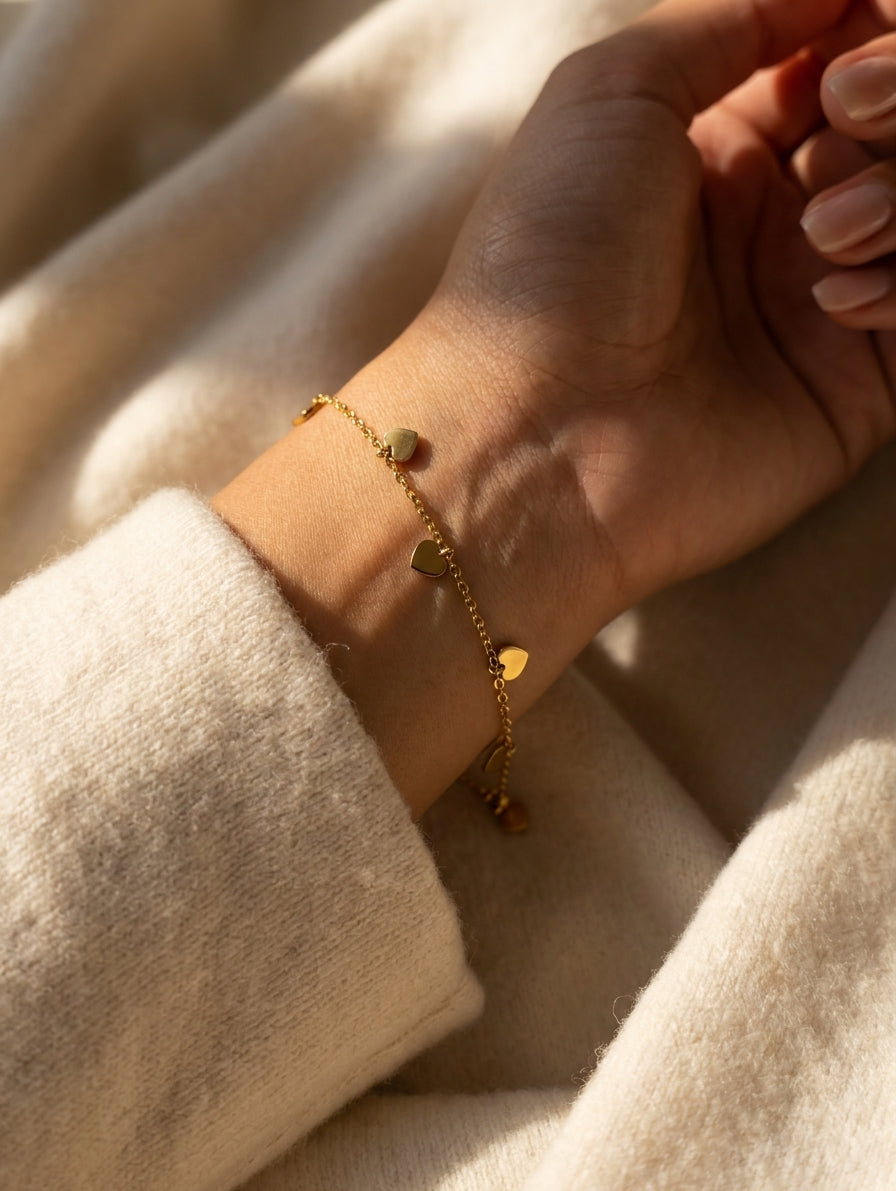 Woman wearing dainty gold multi heart dangle charm bracelet on wrist in cream knit sweater – AureliaBlends
