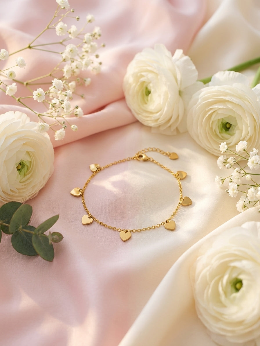 Dainty gold-plated multi heart charm bracelet flat lay on blush pink silk with white ranunculus roses and gypsophila – AureliaBlends