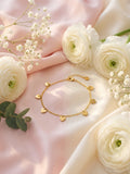Dainty gold-plated multi heart charm bracelet flat lay on blush pink silk with white ranunculus roses and gypsophila – AureliaBlends