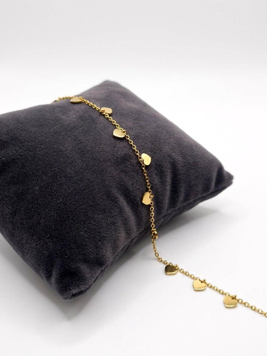 Dainty gold heart dangle charm bracelet draped over dark grey velvet jewelry pillow on white background – AureliaBlends