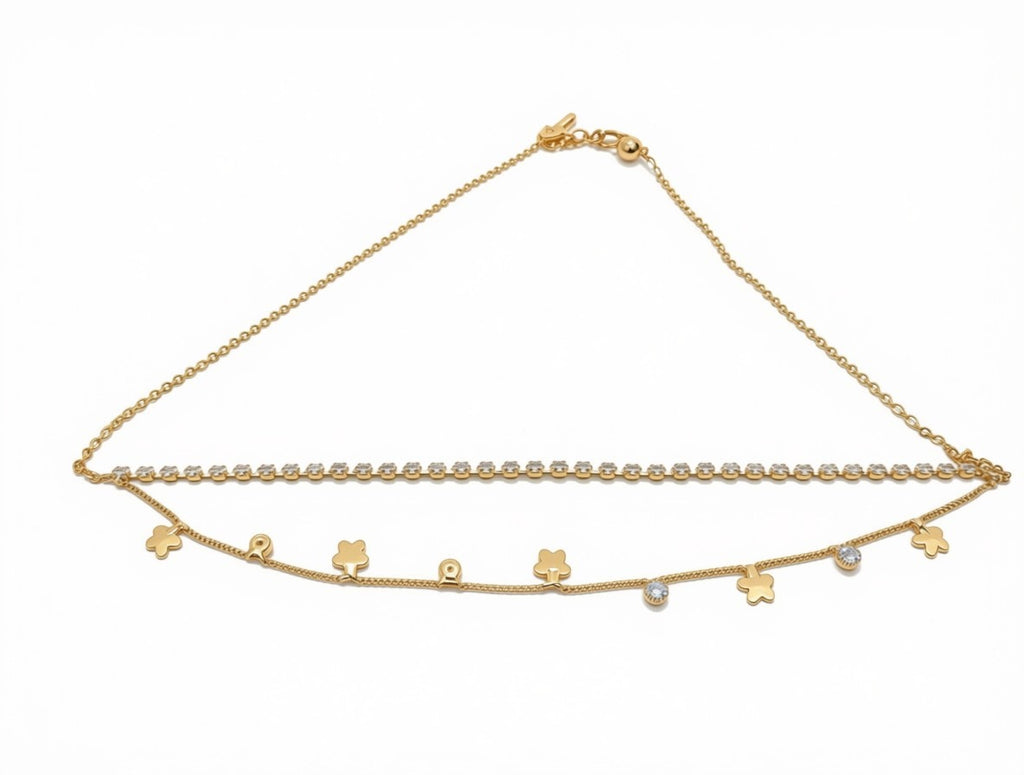 A delicate gold chain anklet featuring a double-strand design, one chain with small clear stones and the other with small gold charms including flowers, a cat silhouette, and a heart, displayed on a white background.