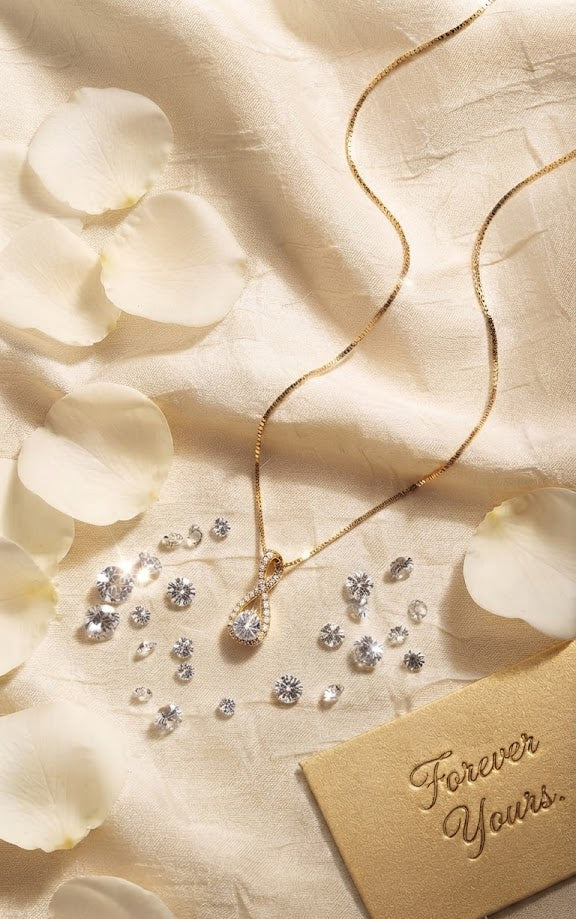 Gold CZ infinity teardrop pendant necklace on black jewelry bust surrounded by pink and red roses with fairy lights – romantic floral display