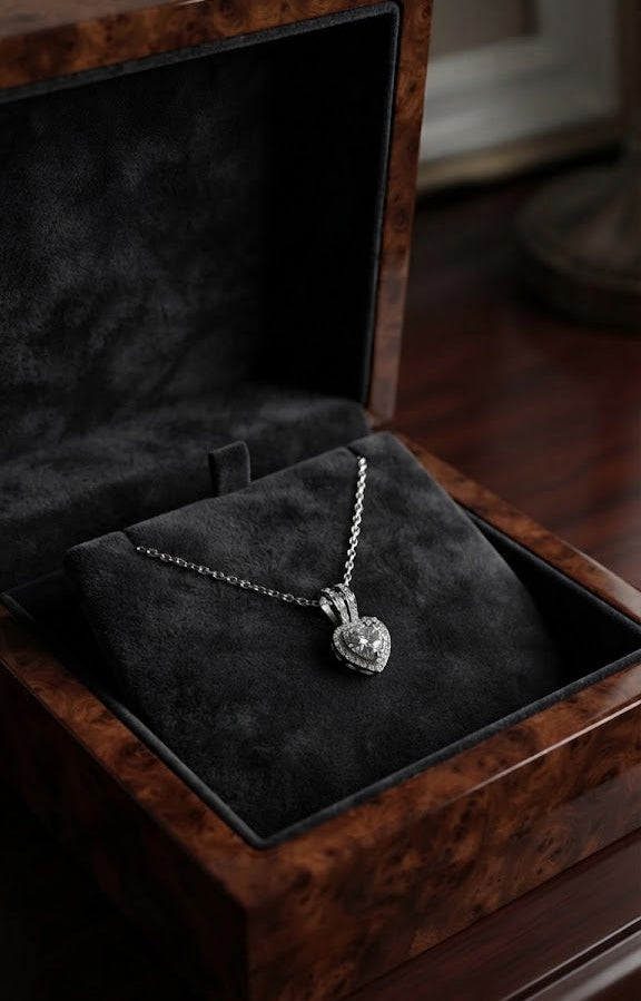 Silver cubic zirconia heart halo pendant necklace flat lay on black surface with gold pen, white envelope with wax seal, silver ribbon and Timeless Elegance card