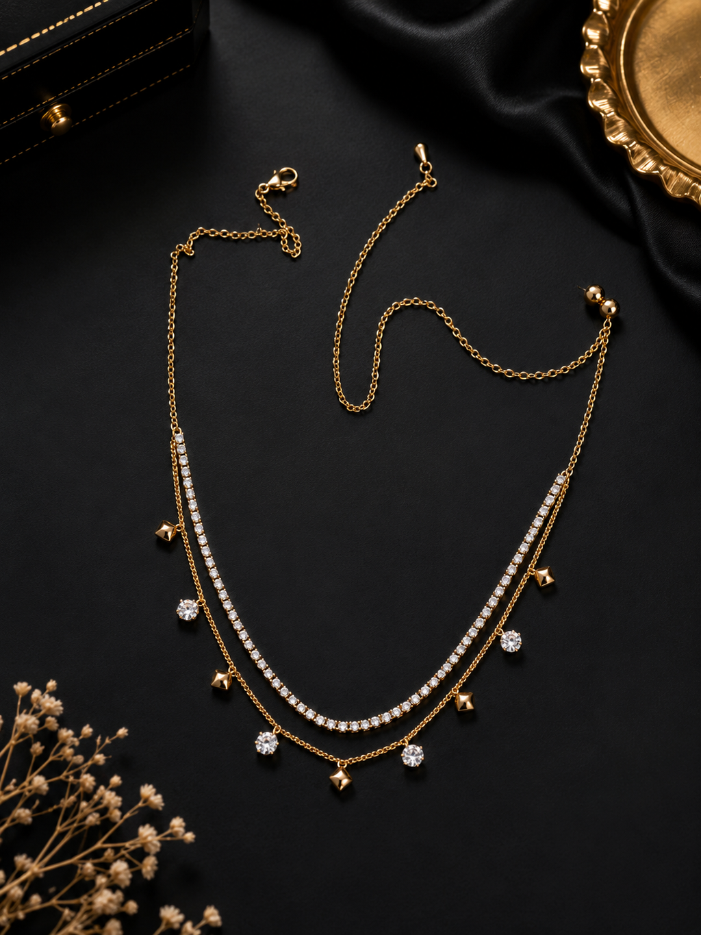Gold double layer CZ tennis necklace and curb chain with CZ bezel and gold pyramid charm dangles flat lay on black background with gold tray and dried flowers – AureliaBlends