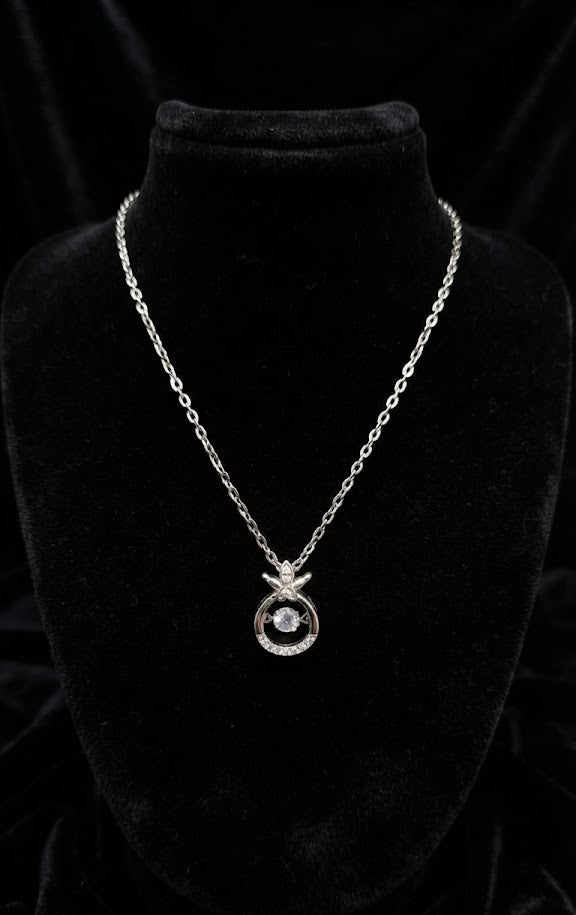 Silver crystal circle pendant necklace close-up showing cubic zirconia centre stone and pavé halo arc with dragonfly charm topper