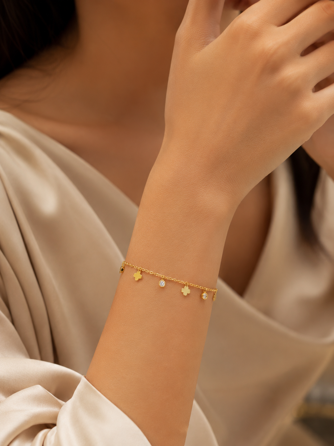 Woman wearing gold clover and CZ dangle charm bracelet on wrist in cream satin dress with white roses – AureliaBlends
