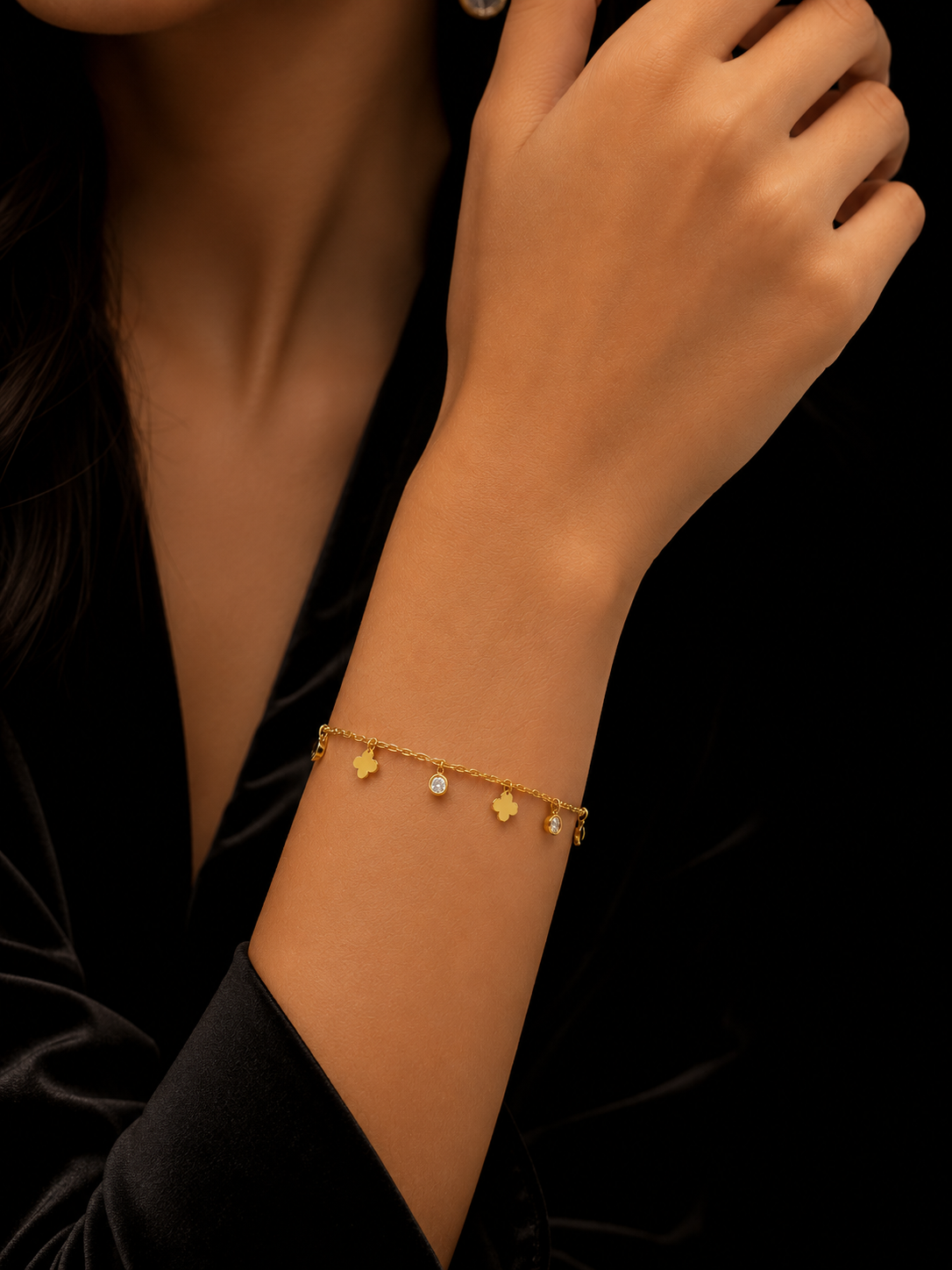 Woman wearing dainty gold four leaf clover and CZ crystal dangle charm bracelet on wrist in black velvet dress – AureliaBlends