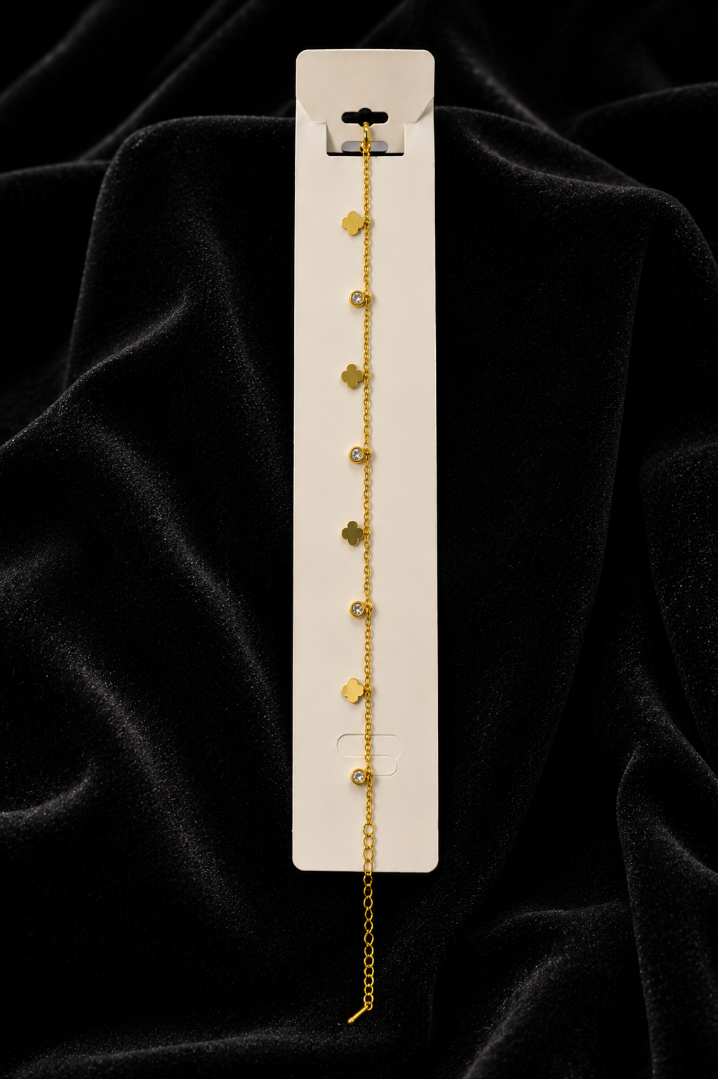 Gold four leaf clover and CZ dangle charm bracelet on white retail card displayed on black velvet background – AureliaBlends