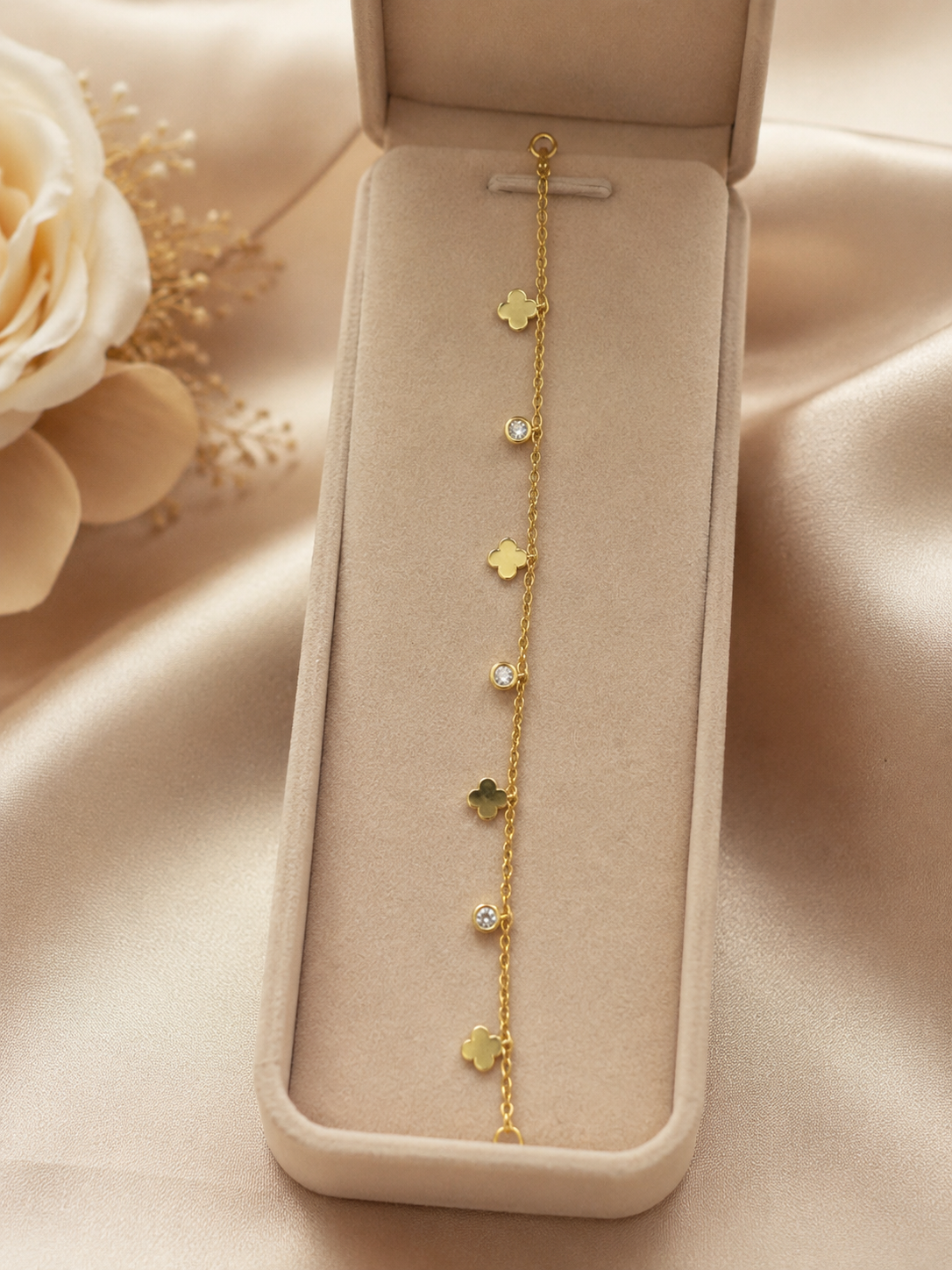 Dainty gold-plated four leaf clover and CZ crystal charm bracelet displayed in beige velvet jewelry box with white roses – AureliaBlends