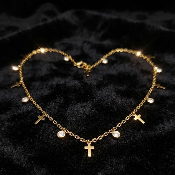 Gold cross charm necklace with crystal drops arranged in heart shape on black velvet fabric