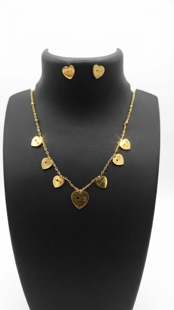 Gold love heart charm necklace and earrings set laid flat on white lace fabric with eucalyptus, ring box and perfume – AureliaBlends