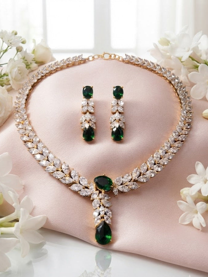 Gold-plated emerald green CZ bridal necklace and earrings set displayed on blush pink silk with white flowers – AureliaBlends
