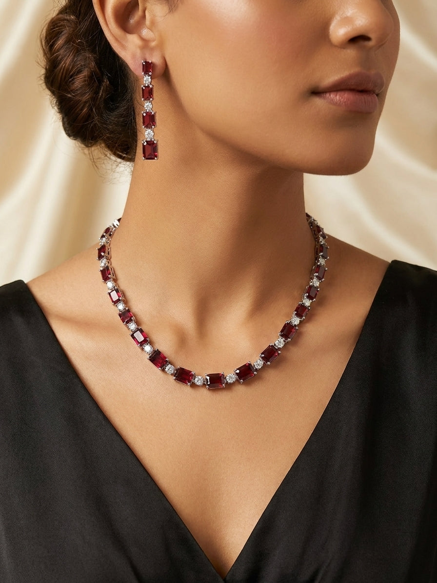 Ruby red CZ tennis necklace and drop earrings bridal set flat lay on black velvet with gold mirror frame and eucalyptus – AureliaBlends