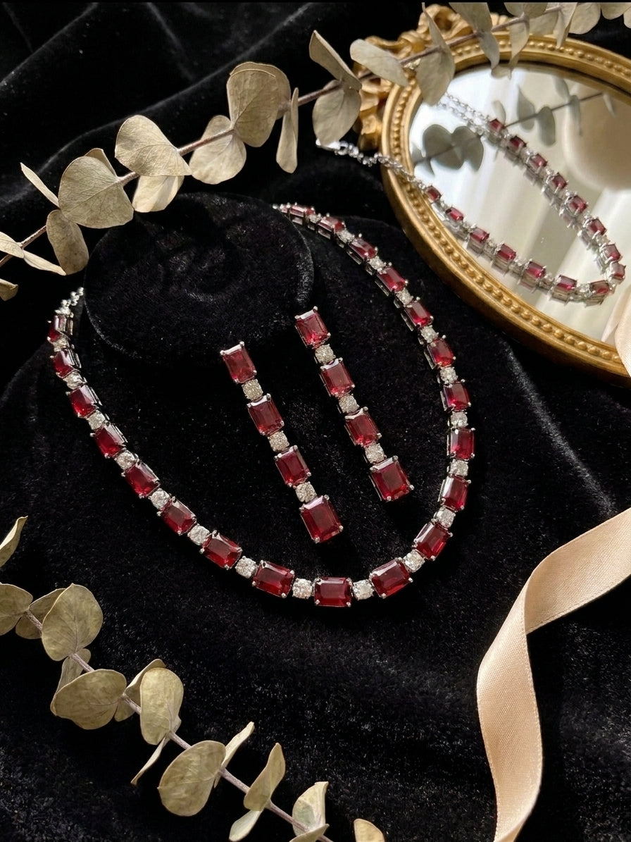 Ruby red emerald cut CZ tennis necklace and drop earrings set displayed in open beige velvet luxury jewelry box with gold hardware on cream satin with orchid flowers – AureliaBlends