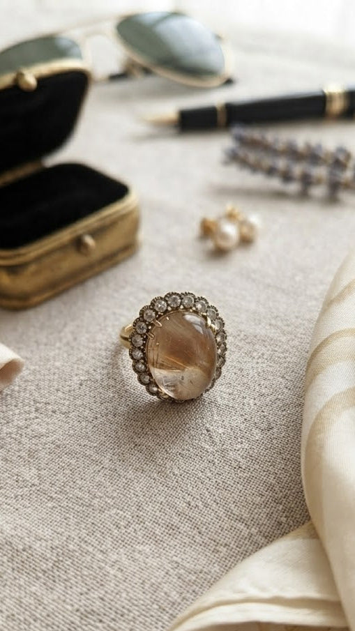 Woman wearing gold oval peach stone CZ halo cocktail statement ring on index finger with neutral manicure in white V-neck top – AureliaBlends