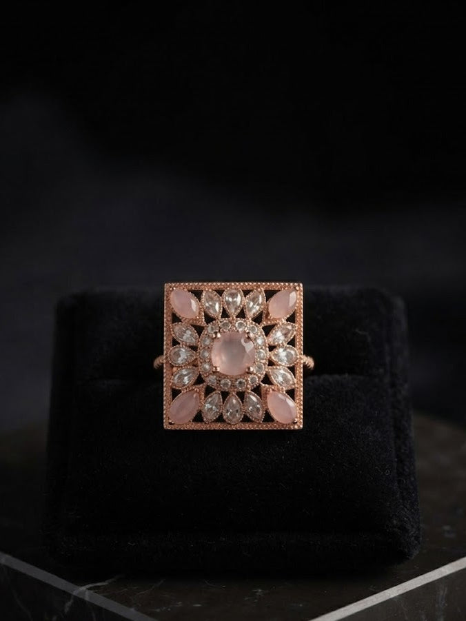 Rose gold square filigree statement ring with pink opal cabochons and CZ pavé milgrain border displayed on white velvet ring cushion on marble surface – AureliaBlends