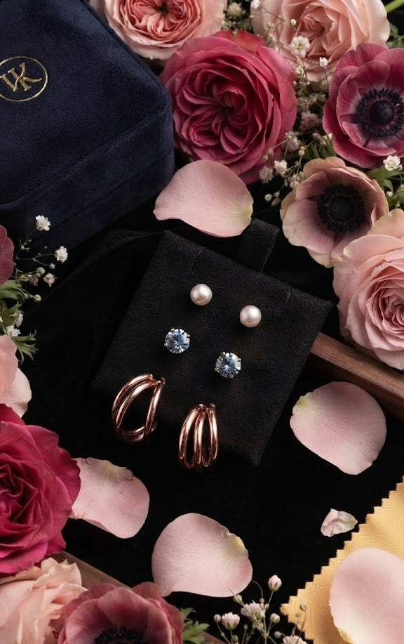AureliaBlends curated earring set with gold hoops, pearl and crystal studs displayed on cream linen with rose petals