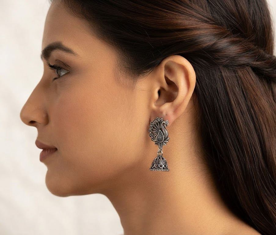 Close-up of oxidized silver peacock jhumka earrings on navy blue velvet – handcrafted antique silver dangle drop earrings AureliaBlends