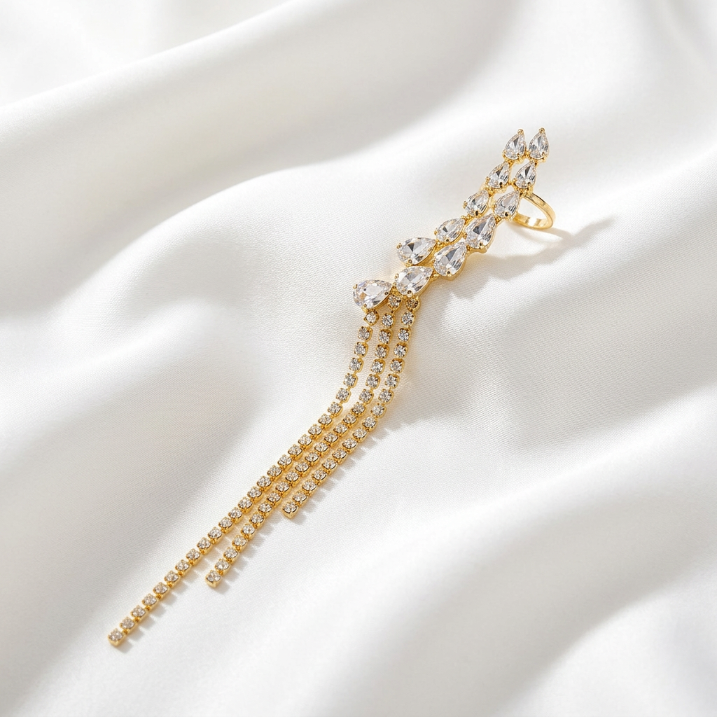 A gold-toned statement ring featuring a cluster of clear teardrop and marquise-cut stones with three dangling chain strands, displayed on draped white satin fabric.