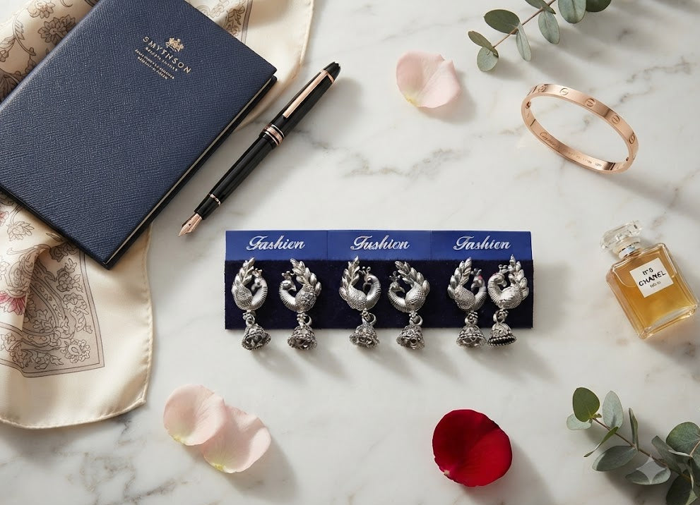 Three pairs of oxidized silver peacock jhumka earrings on marble flat lay with Chanel perfume, rose petals and gold bangle – AureliaBlends lifestyle