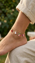 Woman wearing gold-plated double layer fruit charm anklet with strawberry and cherry charms on ankle in linen trousers outdoors – AureliaBlends