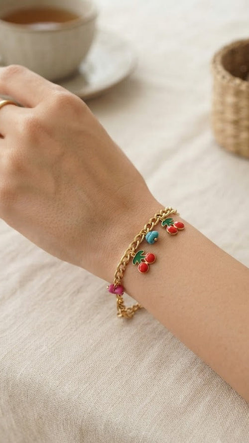 Woman wearing gold cherry charm bracelet with red enamel charms and colorful beads on wrist – AureliaBlends