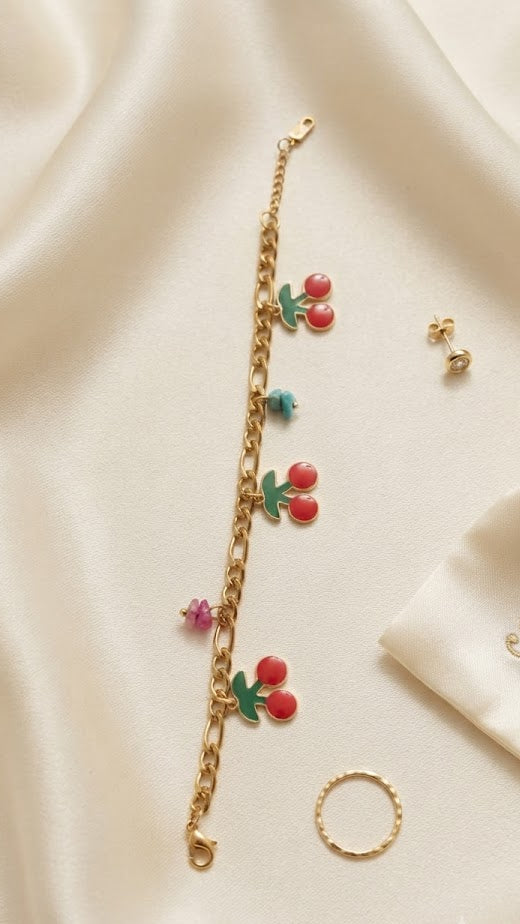 Gold-plated cherry enamel charm bracelet with colorful beads flat lay on cream silk – AureliaBlends