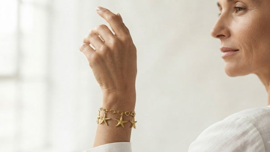 Woman wearing gold starfish charm bracelet on wrist in white linen shirt – AureliaBlends