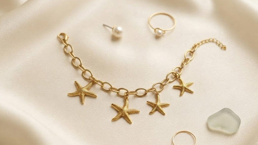 Gold starfish charm bracelet flat lay on cream silk with pearl earrings and gold rings – AureliaBlends