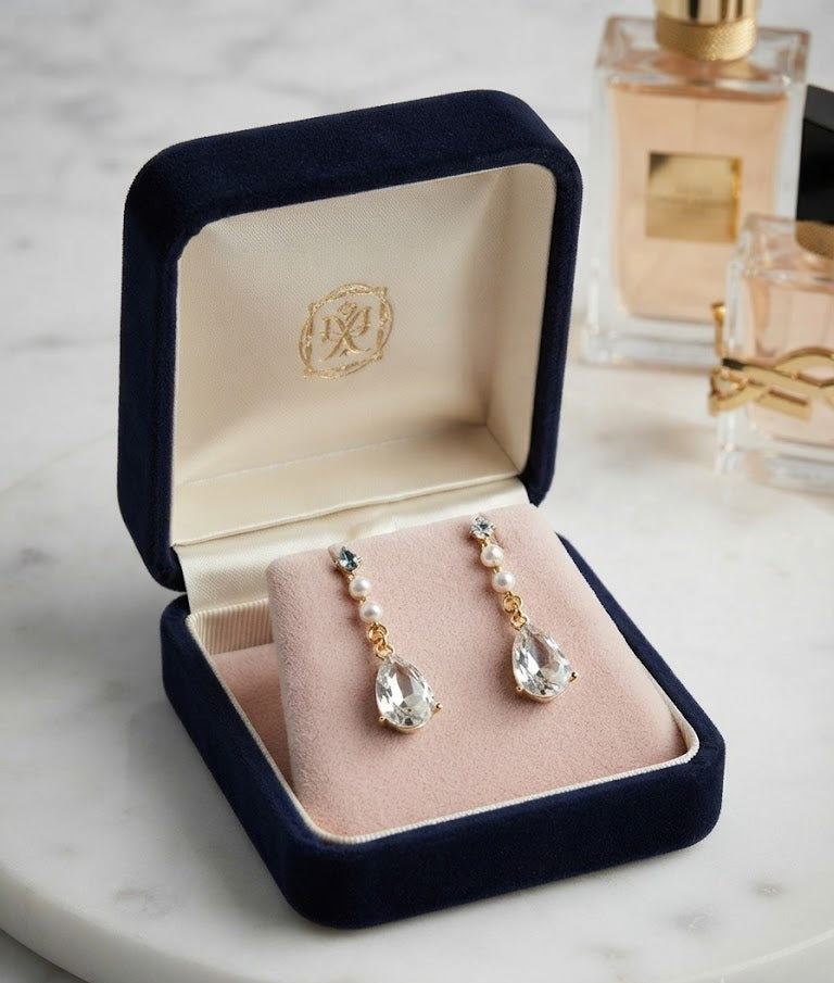 Gold pearl and teardrop crystal drop earrings in open navy blue velvet gift box on marble with perfume and YSL lipstick – AureliaBlends statement earrings