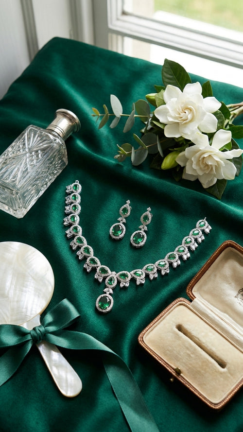 Emerald green CZ necklace and earrings set flat lay on black velvet with white gardenias, crystal decanter and pearl hand mirror – AureliaBlends luxury