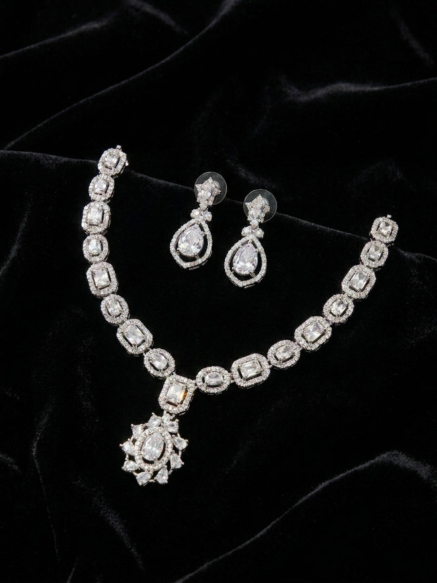 Model wearing silver cubic zirconia bridal necklace and earring set with a navy off-shoulder gown in an elegant interior – AureliaBlends